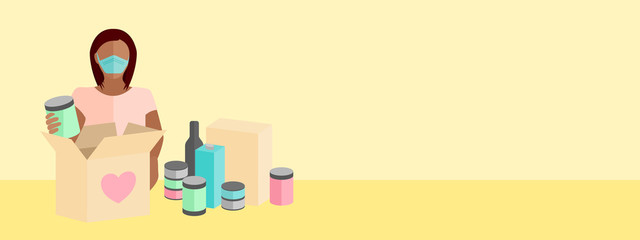 Woman wearing a mask packing a box full of food items to give to those in need of help during the COVID-19 coronavirus pandemic