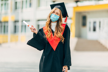 A graduate student in a medical mask, in a black graduation dress, with a diploma in her hands....