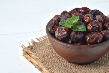 dried date and green mint in a bowl on white wooden table.