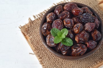 dried date and green mint in a bowl on white wooden table.