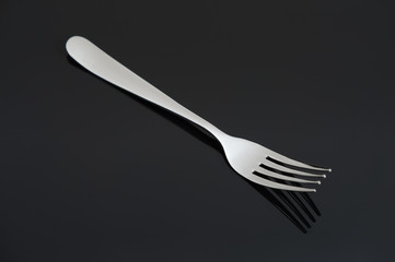 Elegant shiny silver fork on black mirror background.