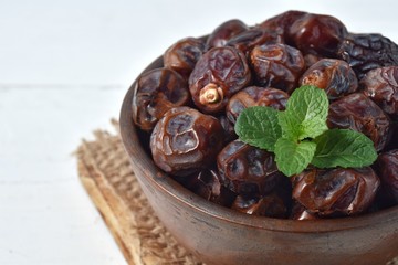 dried date and green mint in a bowl on white wooden table.
