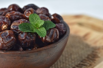dried date and green mint in a bowl on white wooden table.