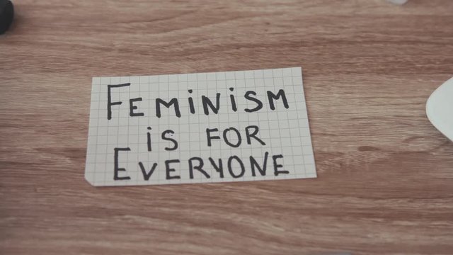 Close up paper on table text Feminism is for Everyone power inside desk woman females feminist girls slow motion