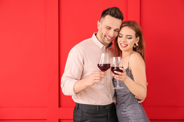 Happy couple with glasses of wine on color background