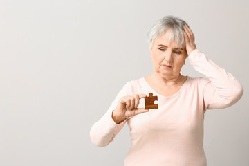 Elderly woman suffering from mental disability with puzzle piece on grey background