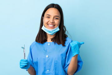 Young brunette mixed race dentist woman holding tools over isolated background with thumbs up gesture and smiling