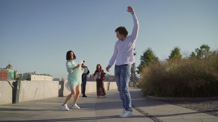 Fototapeta premium A young couple dancing to live music on the street. Musicians play, and a young couple dancing on the promenade. Music street performers couple with girl violinist and man guitarist on blue sky