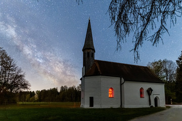 Fototapeta na wymiar One impressive photo of the milky way and its galactical centre next to a chapel with copy space at the top of the long exposure photo.