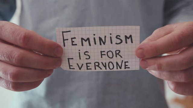 Close up man hands hold paper with text Feminism is for Everyone power inside slow motion