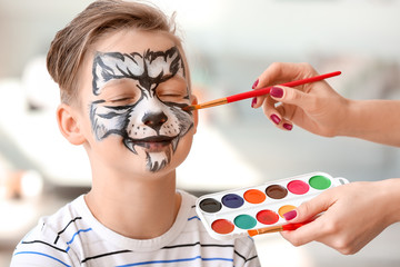 Woman painting face of cute little boy at home