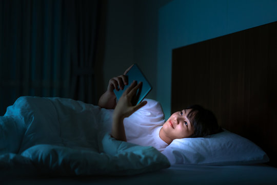 Asian Mobile Addict Woman Using Digital Tablet Browsing The Internet For Watching Movie Or Virtual Meeting Video Call Online With Boyfriend On The Bed Before She Sleeping At Night..