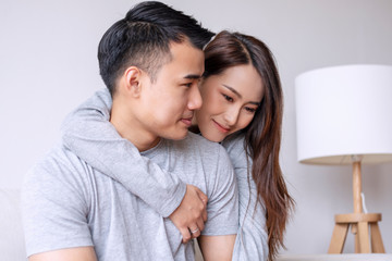 Young woman hugging her boyfriend from back while sitting together on sofa at home. Romantic couple embracing feeling relax in living room. Relationship and valentines day concept.