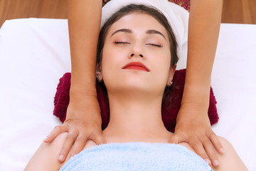 Young woman lying on red towel while receiving massage in spa salon with masseuse hands. Relax girl getting treatment on her body enjoying at spa.