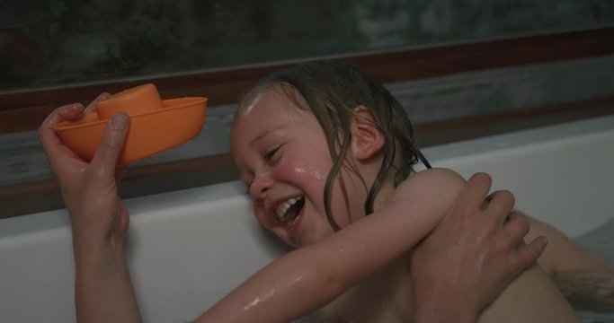 Preschooler in bathtub with mother moving away from hair wash