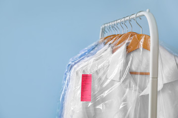 Rack with clothes after dry-cleaning on color background