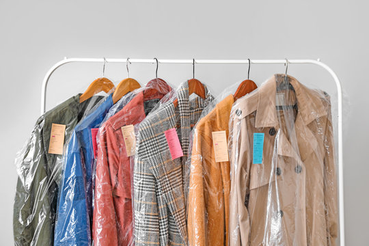 Rack with clothes after dry-cleaning on light background