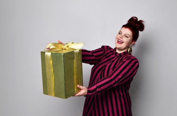 Happy ginger woman in black and purple striped dress, crown and earrings. Holding golden gift box...