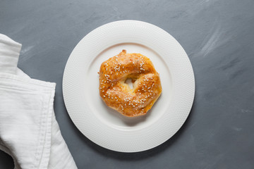 Homemade baking. Delicious gluten free ring with sesame seeds on a white plate. Gray structural background. Top view, close-up. Copy space