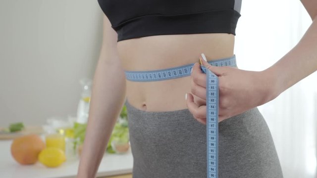 Young slender Caucasian girl measuring waist. Unrecognizable slim woman in sportswear controlling weight. Sportive thin lady dieting. Healthy lifestyle, beauty standard, grace.