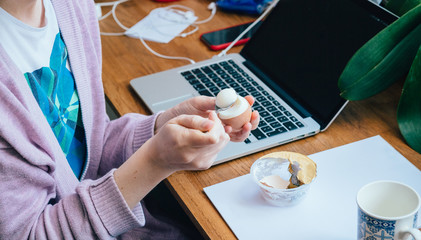 Teleworking workday from home concept with woman eating boiled egg typing working laptop during coronavirus worldwide confinement pandemic