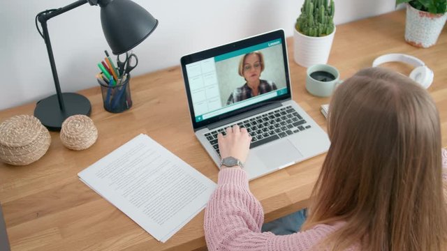 Female Student Study Online and Learns Video Lesson with Teacher using Laptop at Home. E-learning Classe, Webinar, Distance course or Workshop concept at COVID-19 Pandemic. 4K Top View Orbit Shot