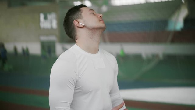 Young athlete male wears wireless headphone and stretches before sports exercise