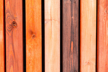 A rustic wooden fence made from crafted multi-colored narrow planks. Vertical background wall made of vintage pine wood in vintage style.