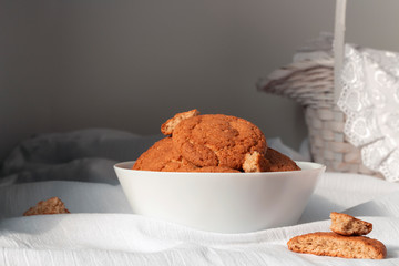 Homemade oatmeal cookies in white dishware on white fabric tablecloth