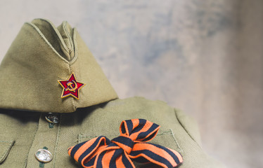 May 9 greeting card, Victory day 1945 holiday background. Forage cap with Red Army star and St. George ribbon lying on Soviet army military tunic uniform. Layout, copy space.
