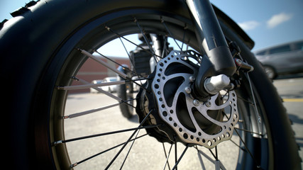 Fototapeta premium Focus on the tire of the electric bicycle with wheel motor at sunny summer day and light leaks and asphalt on the background. E bike motor with sun reflections on the parking near store. Close up.