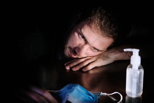 a doctor exhausted resting on the table at night quarantine lockdown for social distancing with the cellphone screen lighting , the chinstrap and the gel alcohol during the covid-19 pandemic