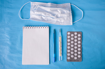 Notepad, pen, medical mask, tablets, thermometer on a blue background