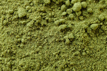 Dried powdered wheat grass showing fine green texture and granule bits, closeup macro top view. Processed wheatgrass in powder form, a health supplement rich in vitamins, minerals and amino acids.