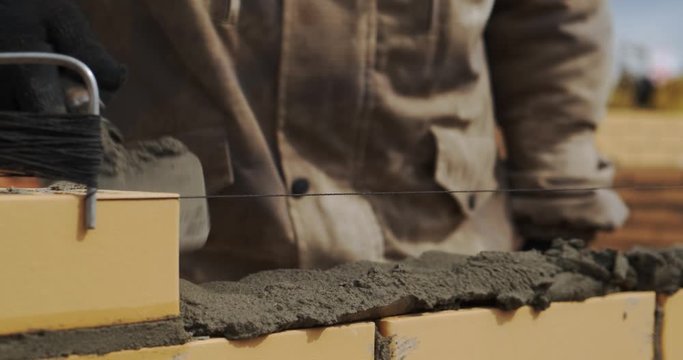 Builder puts mortar. Worker trowel puts cement on brick. High-quality construction of building. Builder glues brick. Bricklayer is building wall. Construction is men's work. Mason builds wall. Masonry