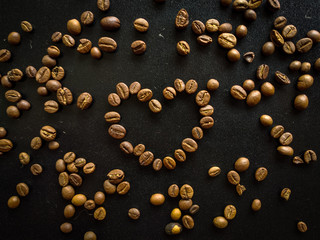 Coffee beans in heart shape on black rustic wooden background, love of coffee, symbol of love. Roasted coffee beans.