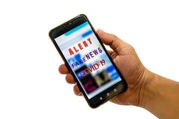 Hand holding a smartphone with 'fakenews' message on the phone screen. Concept photo for Covid-19 pandemic.