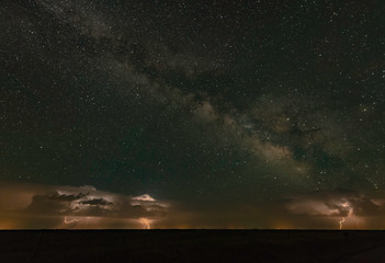 Fototapeta premium A distant supercell thunderstorm is throwing lightning bolts with the milky way overhead.