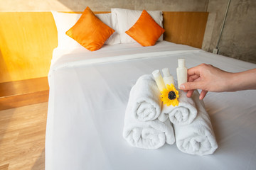 Close up of Hotel maid hand putting flower and arranging the set of towels with treatment shampoo on bed. Conceptual of female chambermaid making bed in hotel room.