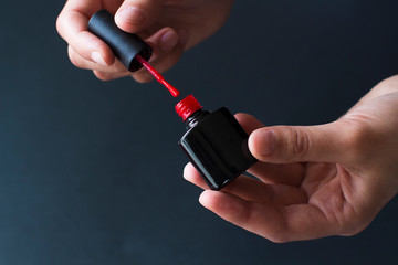 young woman making manicure herself using red nail polish on black background. holding a black bottle of red nail polish in her hands