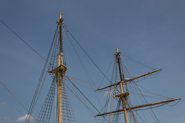Two masts, rigging and shrouds on an old tall ship against a blue sky, horizontal aspect