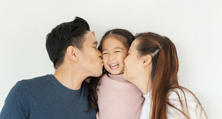 Happy Asian family. Young Father and Mother kiss in their daughter cheek together.