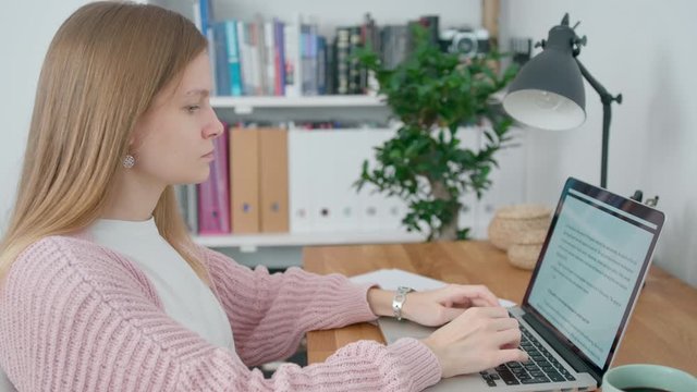 Young Woman Works in Home Office using Laptop. Female Student or Copywriter is Typing in Text Editor at Daytime. Self-isolation concept at Coronavirus Pandemic. 4K Medium Orbit Shot