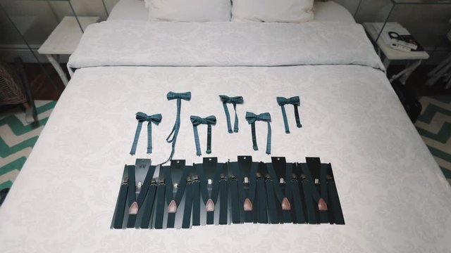 Bowties for the groom and best men on the bed and suspenders, front view of grooms accessories, wedding preparation