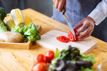 Closeup image of a woman chef cutting and chopping tomato by knife on wooden board