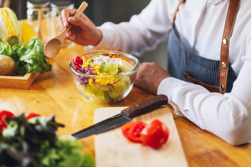 Closeup image of a female chef cooking and eating a bowl of fresh mixed vegetables salad in kitchen