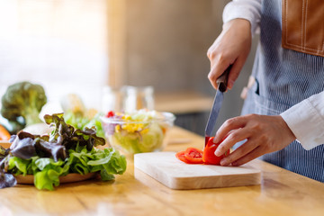 Closeup image of a woman chef cutting and chopping tomato by knife on wooden board