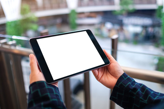 Mockup image of a woman holding black tablet pc with blank white desktop screen indoors