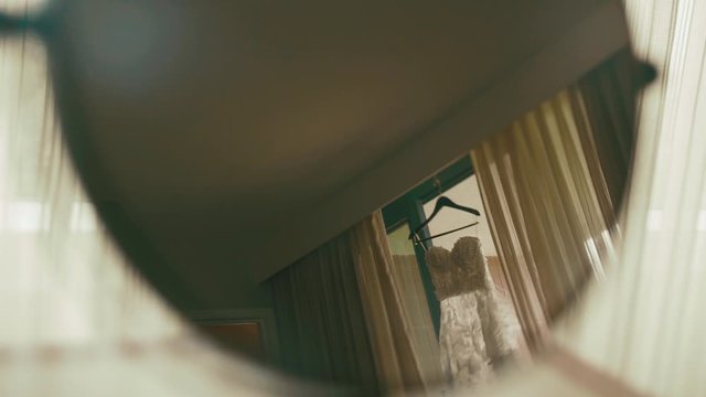 Reflection of beautiful wedding dress which is hanging on the window between curtains in the room in the mirror, wedding day, wedding clothing