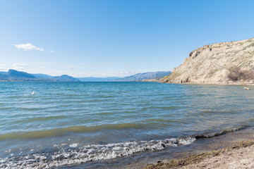 Fototapeta na wymiar Scenic view of Okanagan Lake, sandstone cliffs, blue sky and mountains